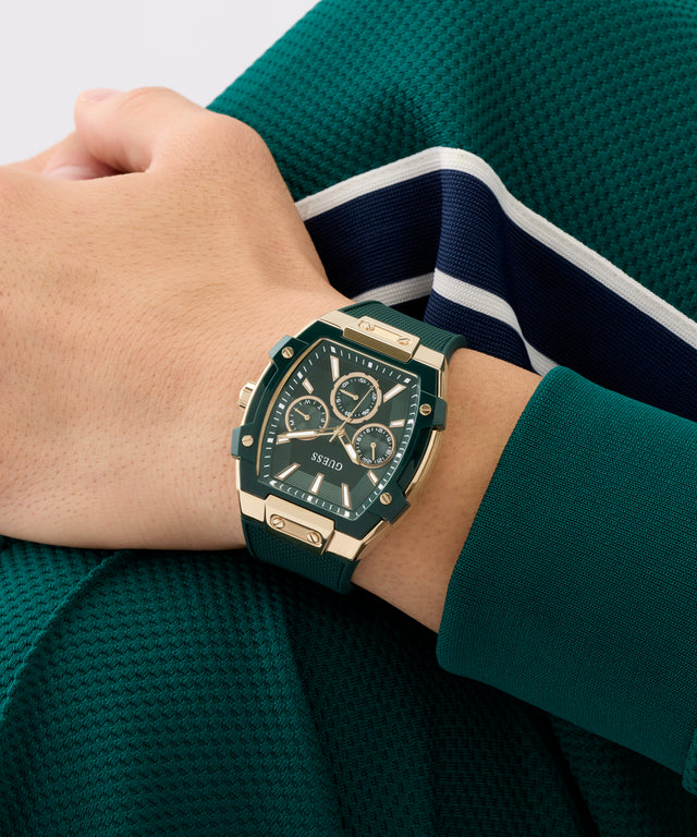 Person wearing a green and gold GUESS Mens Green Rose Gold Tone Multifunction Watch on a green background