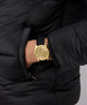 Gold GUESS Mens Black Gold Tone Multi-function Watch on a wrist with a black strap against a black background