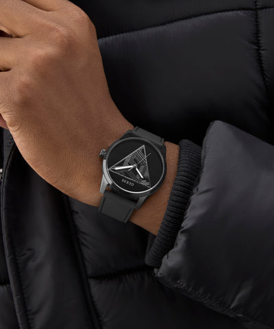 Person wearing a black GUESS Mens Black Analog Watch with a geometric design on a black jacket.