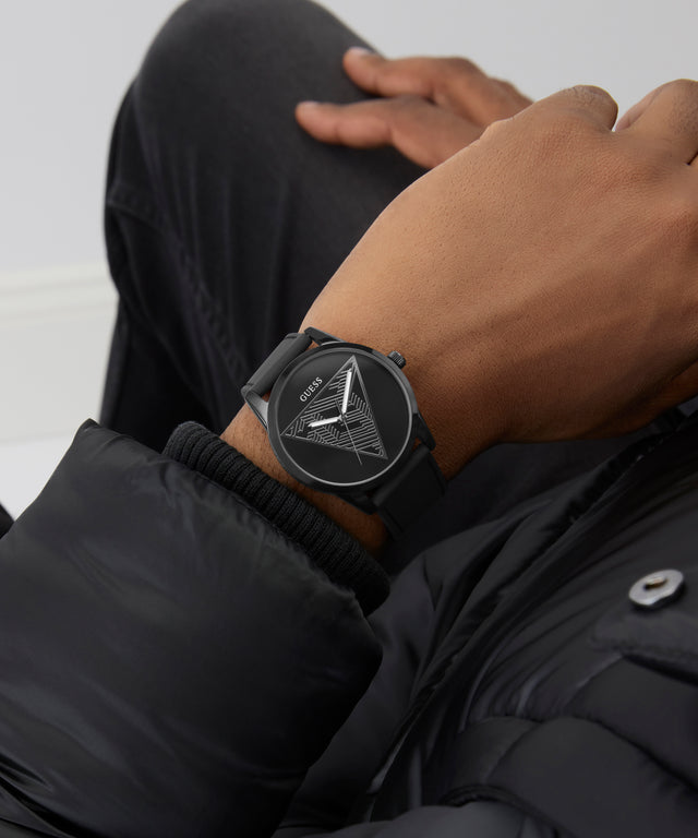 Person wearing a black GUESS Mens Black Analog Watch with a geometric design on a plain background