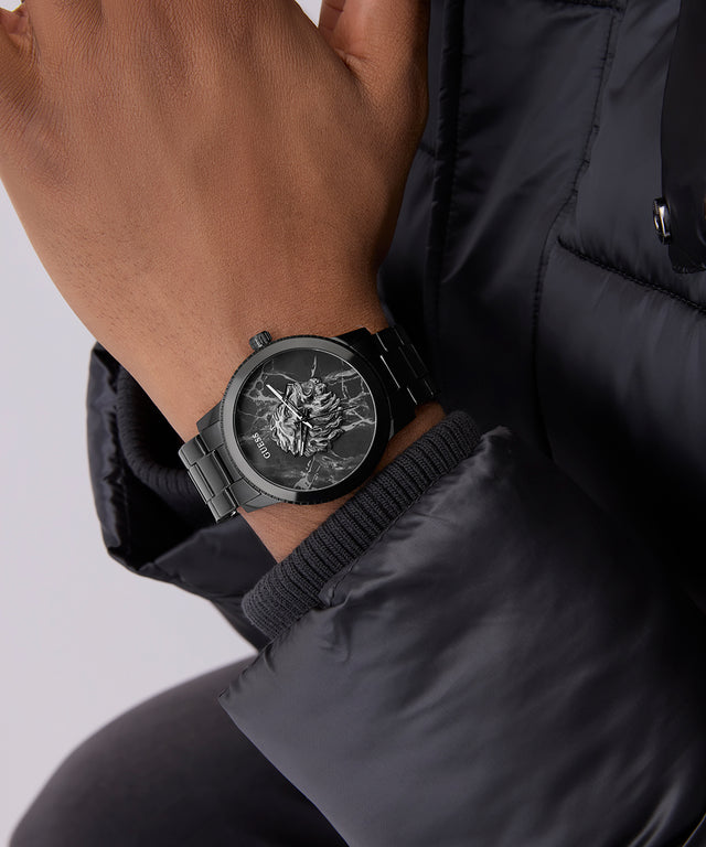 Black wristwatch with detailed design on a person wearing a black jacket against a light gray background