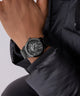 Black wristwatch with detailed design on a person wearing a black jacket against a light gray background