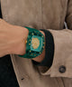 Person wearing a GUESS Mens Green Analog Watch with a gold emblem on a beige jacket.