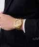 Gold GUESS Mens Gold Tone Multi-function Watch on a person wearing a black suit with a white shirt.