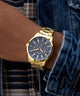 Gold watch on a wrist with a plaid shirt and denim jacket in the background
