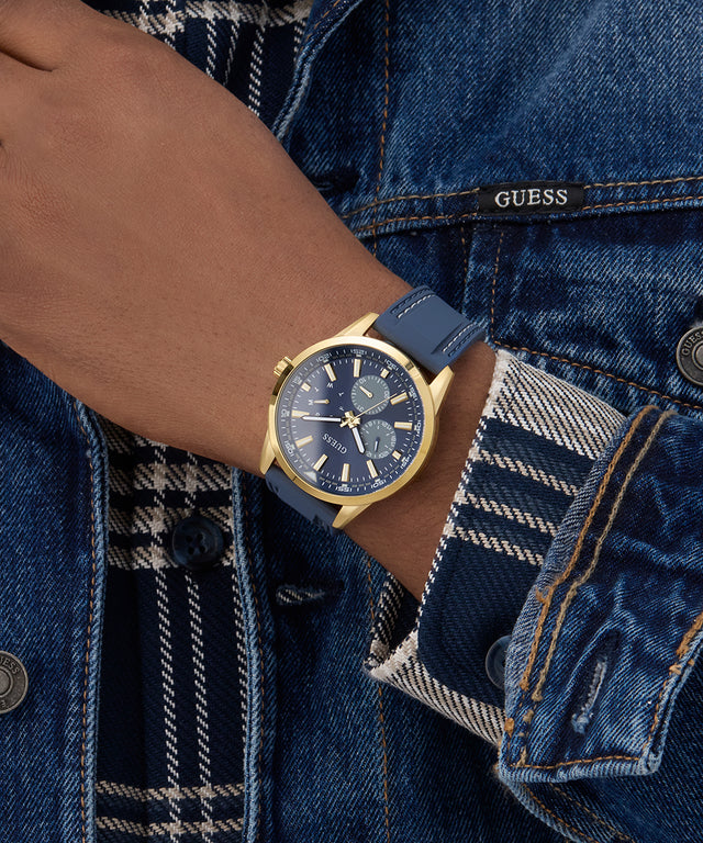 Person wearing a blue watch with gold accents on a denim jacket. GUESS Mens Blue Gold Tone Multi-function Watch GW0964G2