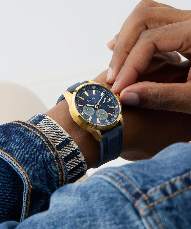 Person wearing a gold and blue watch on a light background GUESS Mens Blue Gold Tone Multi-function Watch GW0964G2