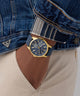 Blue watch with gold accents on a person wearing a denim jacket and beige pants. GUESS Mens Blue Gold Tone Multi-function Watch GW0964G2