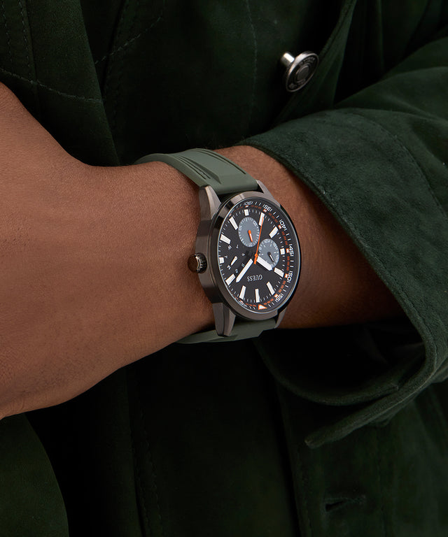 Person wearing a watch with a green strap and dark face, set against a dark background. GW0964G3