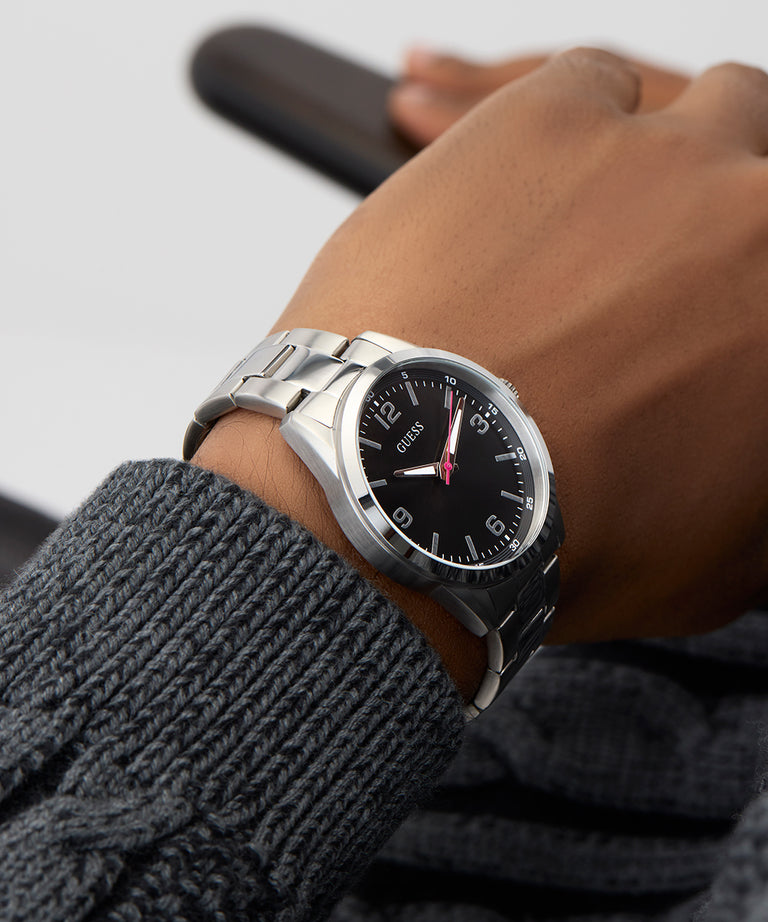 Person wearing aGUESS Mens Silver Tone Analog Watch with a black face on a gray background
