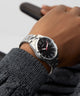 Person wearing aGUESS Mens Silver Tone Analog Watch with a black face on a gray background