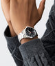 GUESS Mens Silver Tone Analog Watch on a wrist with a gray textured sleeve against a light background