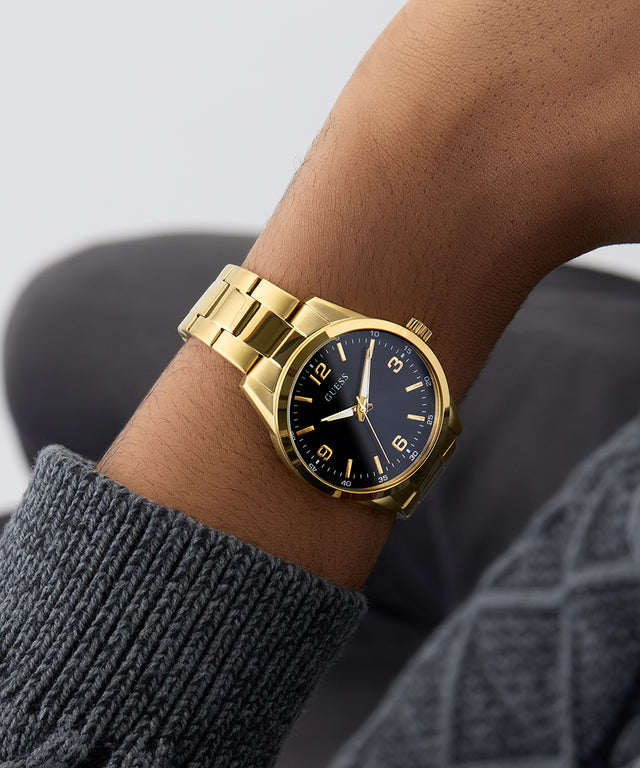 Gold wristwatch with a dark face on a person's wrist against a neutral background GW0965G2
