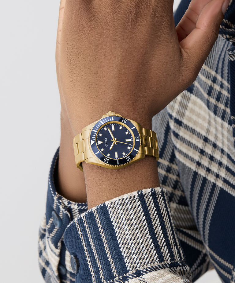 Gold GUESS Mens Gold Tone Analog Watch with blue face on a wrist, wearing a plaid shirt