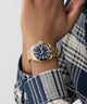 Gold GUESS Mens Gold Tone Analog Watch with blue face on a wrist, wearing a plaid shirt