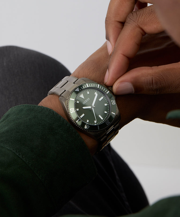 Person adjusting a GUESS Mens Gunmetal Analog Watch on their wrist with a neutral background