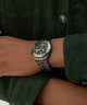 Person wearing a GUESS Mens Gunmetal Analog Watch on a wrist with a green jacket.