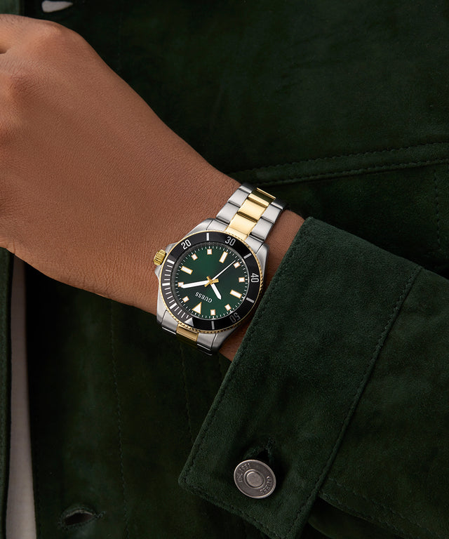 Person wearing a two-tone watch with a green face on a dark background