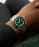 Close-up of a wrist wearing a GUESS Mens 2-Tone Analog Watch with a green face and gold accents.