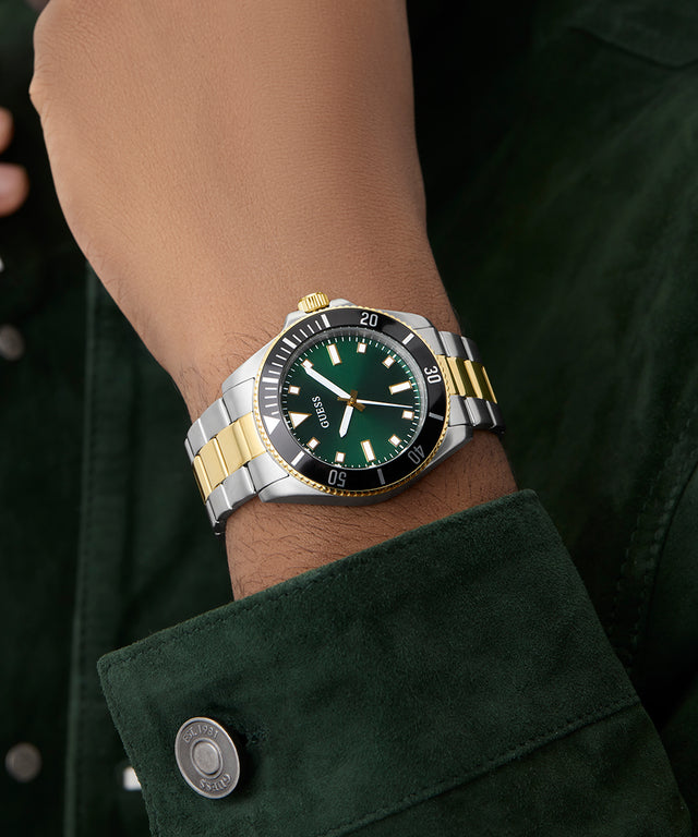 Close-up of a wrist wearing a GUESS Mens 2-Tone Analog Watch with a green face.