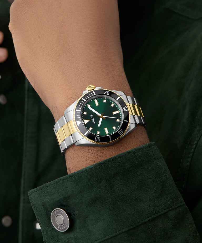 Close-up of a wrist wearing a GUESS Mens 2-Tone Analog Watch with a green face.