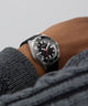 Close-up of a person wearing a black and silver GUESS Mens Black Silver Tone Analog Watch with a gray sleeve.
