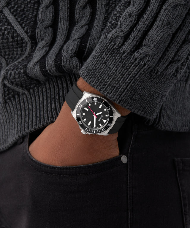 Black GUESS Mens Black Silver Tone Analog Watch on a person wearing a dark sweater and black pants