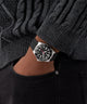 Black GUESS Mens Black Silver Tone Analog Watch on a person wearing a dark sweater and black pants