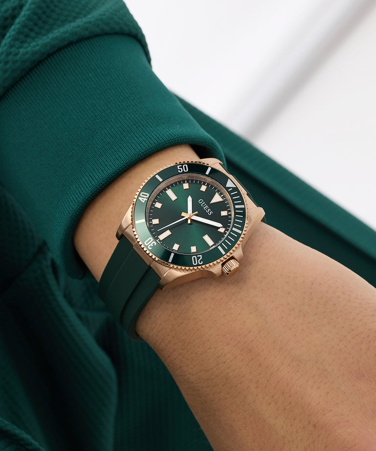 Green GUESS Mens Green Rose Gold Tone Analog Watch on a wrist with a blurred background