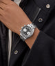 Silver GUESS Mens Silver Tone Multi-function Watch on a wrist with a dark coat background