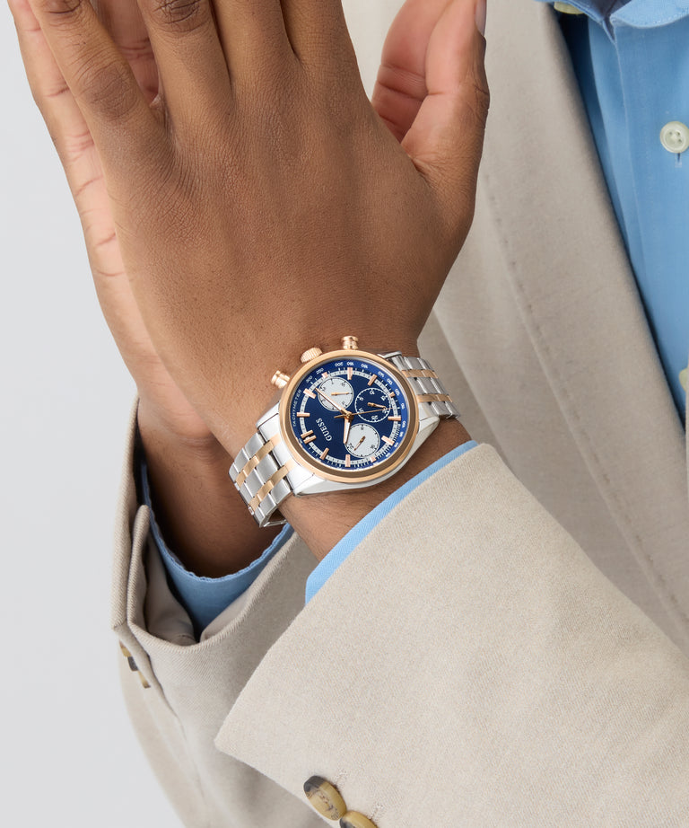 Close-up of a hand wearing a silver and blue GUESS Mens 2-Tone Multi-function Watch with a light gray background