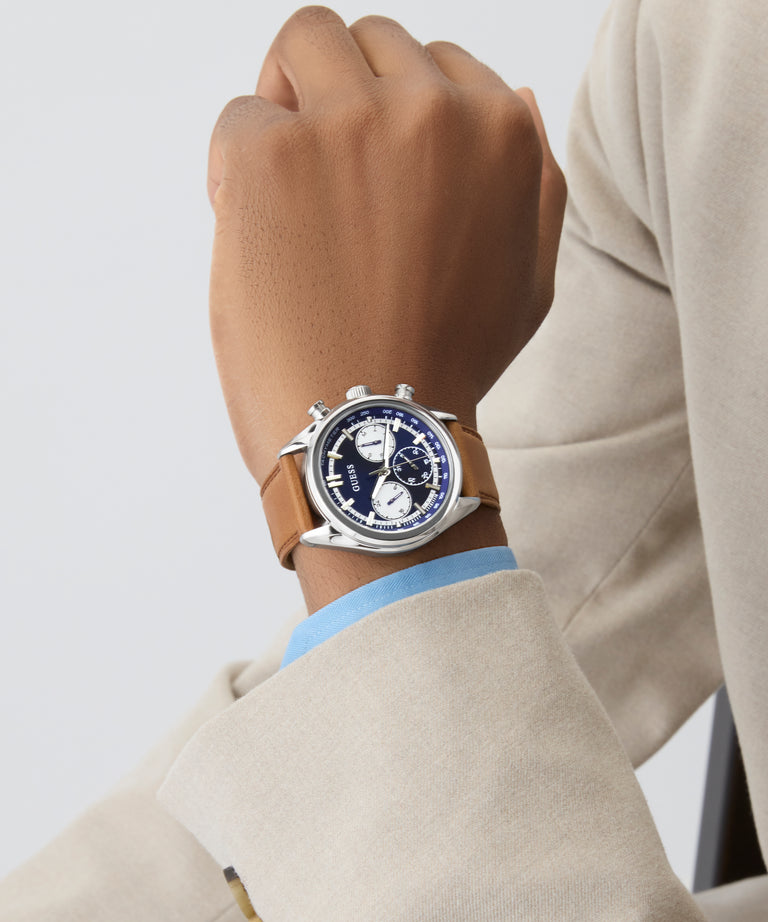Hand wearing a watch with a beige suit and light blue shirt on a plain background GW0972G1