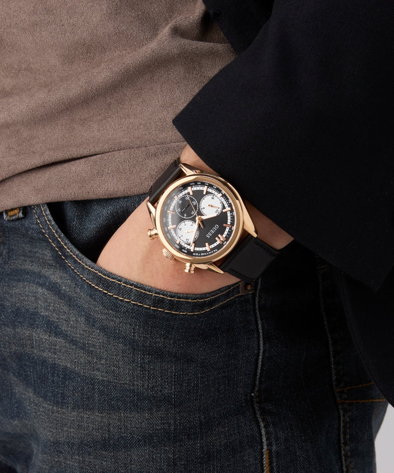 Person wearing a gold GUESS Mens Black Rose Gold Tone Multi-function Watch with a black strap on a neutral background