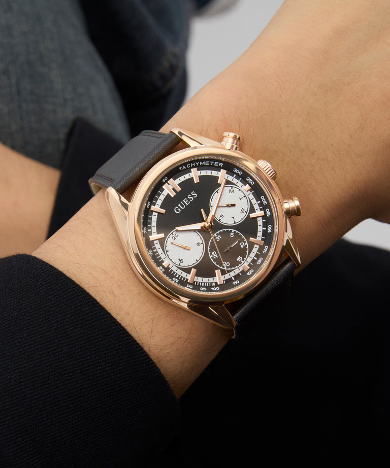 Close-up of a person's wrist wearing a Guess GUESS Mens Black Rose Gold Tone Multi-function Watch with a black strap.