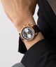 GUESS Mens Black Rose Gold Tone Multi-function Watch with black dial and gold case on a wrist against a neutral background