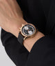GUESS Mens Black Rose Gold Tone Multi-function Watch with black strap and gold case on a person's wrist against a black background
