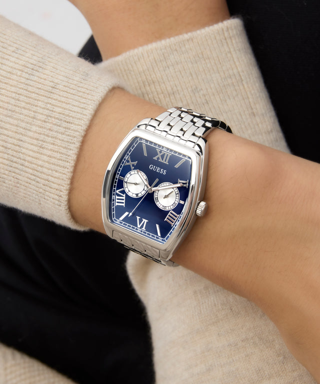 Close-up of a person wearing a GUESS Mens Silver Tone Multi-function Watch watch with a blue face and silver case.