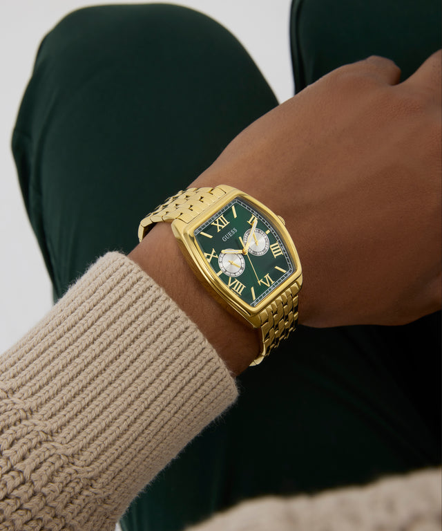 Gold wristwatch with a green face on a wrist, wearing a beige sweater. GW0975G2