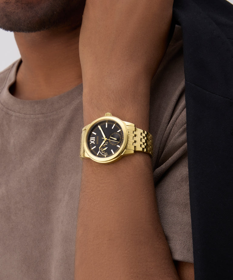 Gold GUESS Mens Gold Tone Multi-function Watch on a wrist with a neutral background