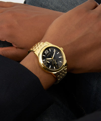 Gold GUESS Mens Gold Tone Multi-function Watch on a person's wrist with a blurred background