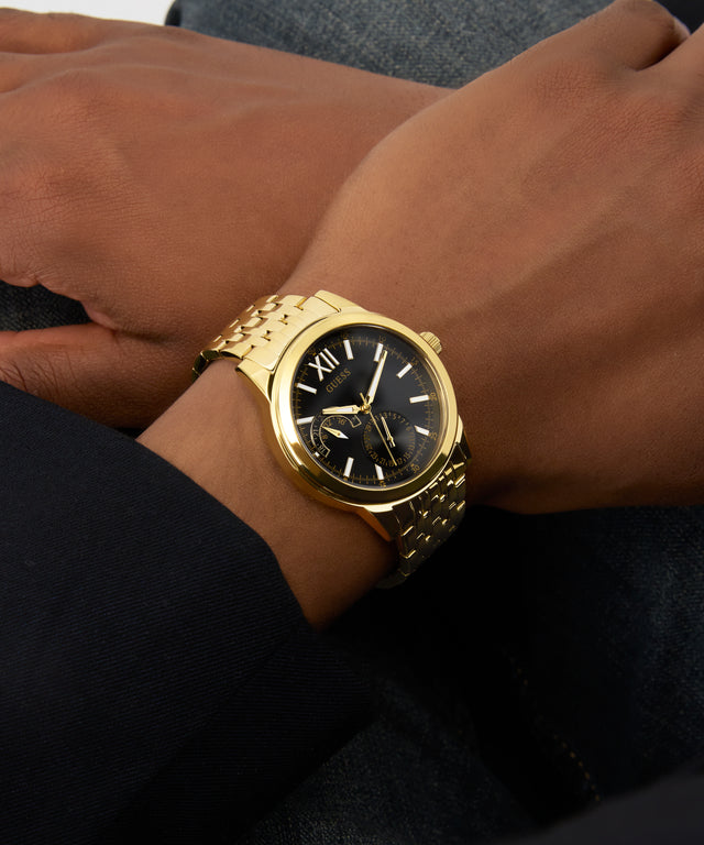 Gold GUESS Mens Gold Tone Multi-function Watch on a person's wrist with a blurred background