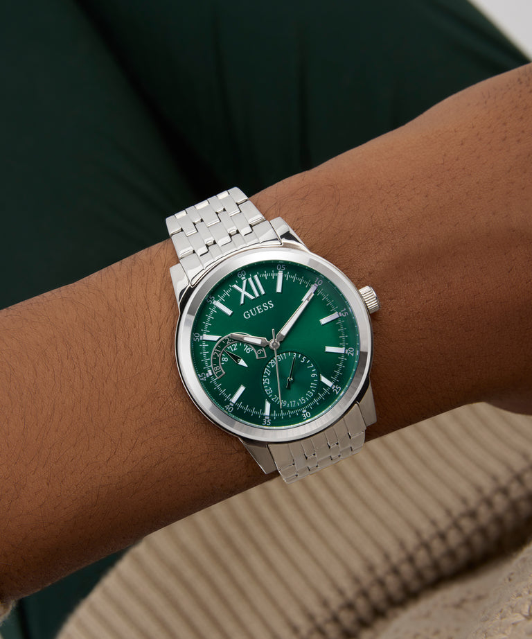Green GUESS Mens Silver Tone Multi-function Watch with silver case and band on a wrist against a neutral background