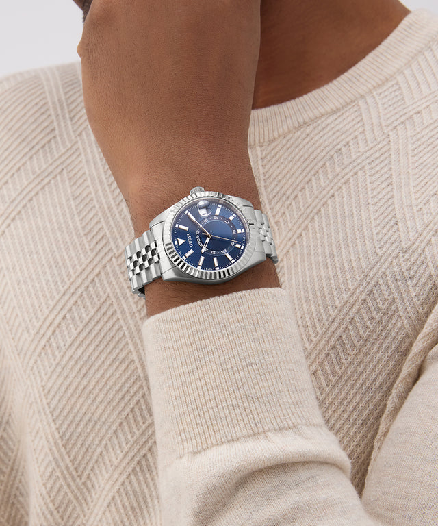 Person wearing a GUESS Mens Silver Tone Multi-function Date Watch with a blue face on a beige sweater.