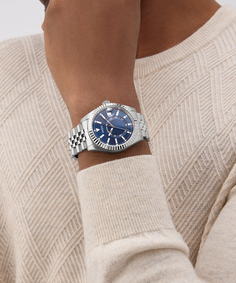 Person wearing a GUESS Mens Silver Tone Multi-function Date Watch with a blue face on a beige sweater.
