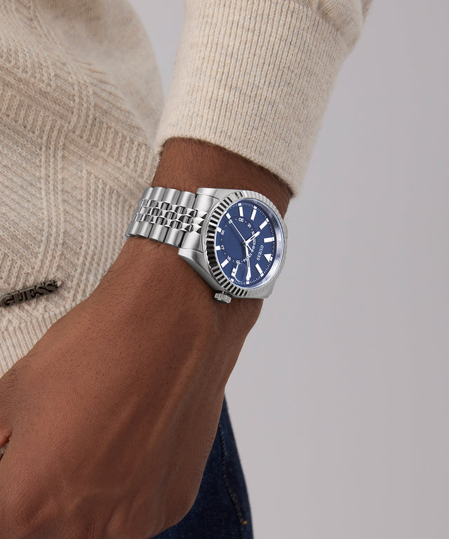 GUESS Mens Silver Tone Multi-function Date Watch with a blue face on a wrist against a neutral background