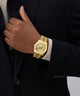 GUESS Mens Gold Tone Multi-function Date Watch on a person's wrist with a dark suit and light shirt.