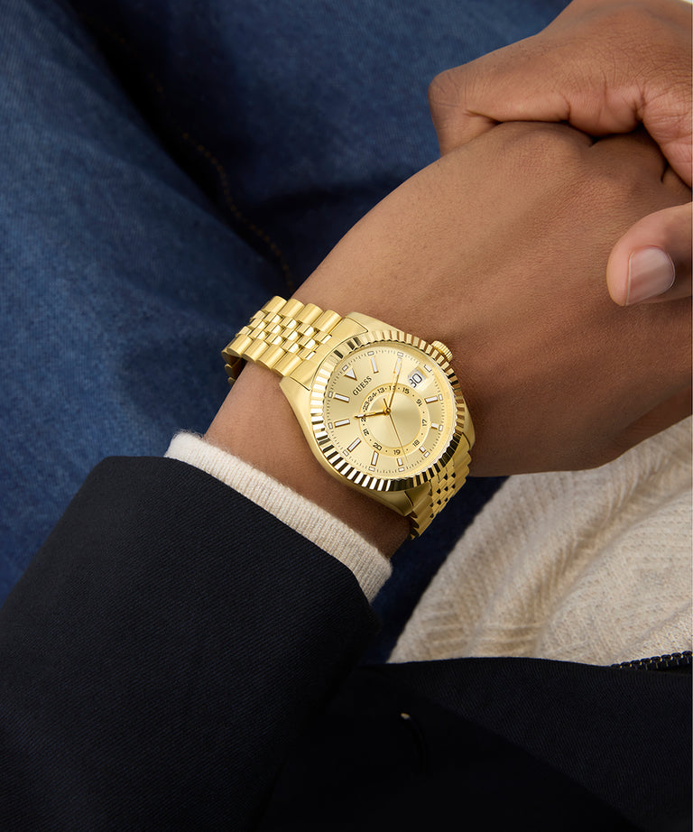 Gold GUESS Mens Gold Tone Multi-function Date Watch on a person's wrist with a blurred background
