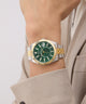 Gold and silver watch with green face on a wrist against a neutral background GW0977G4