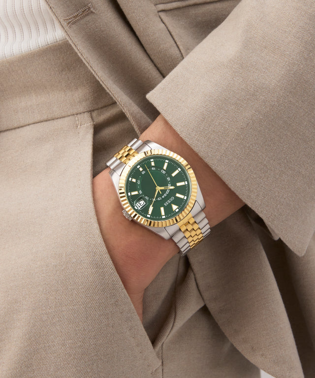 Gold and silver watch with green face on a wrist wearing a beige suit. GW0977G4