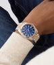 Wrist wearing a two-tone watch with a blue face, close-up on a neutral background GW0977G5